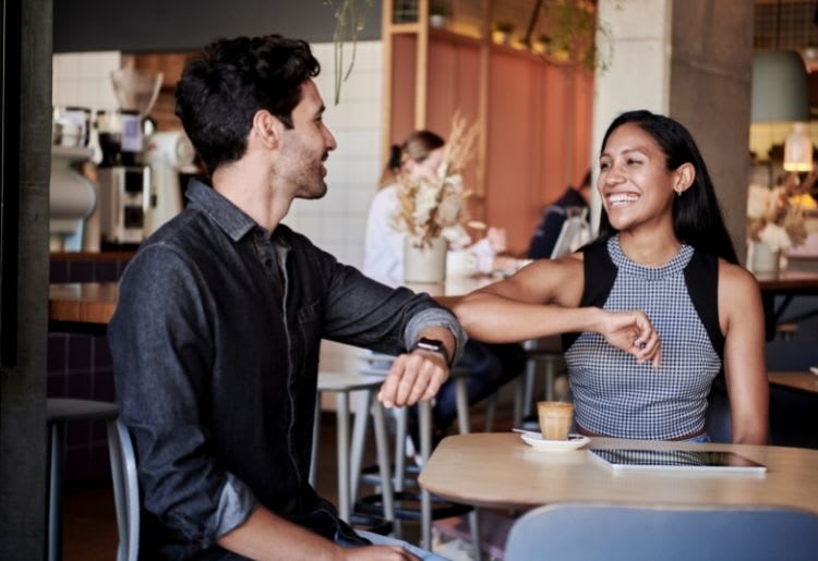A young man and woman greet each other on a date with an elbow touch